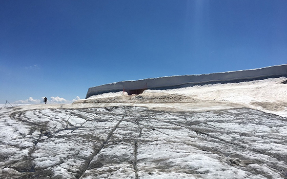 Das Bild zeigt einen Gletscher mit einer sehr dünnen Eishülle, auf der ein sehr grosses und langes Schneereservoir aufbewahrt wird, welches mit einer weissen Plane umhüllt ist. 