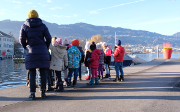 Un groupe d'enfants accompagné d'une animatrice regardent le paysage bâti qui se trouve sur l’autre rive du lac.