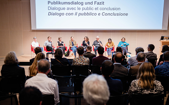 I sette conduttori dei workshop sono seduti con il facilitatore sul palco di fronte al pubblico dell'auditorium