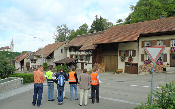Das Bild zeigt eine Gruppe von Inventarisatorinnen und Inventarisatoren bei der Begutachtung einer Häuserzeile in einem Dorf im Kanton Aargau. 